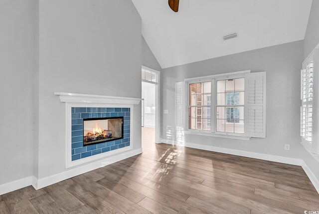 unfurnished living room featuring a tiled fireplace, high vaulted ceiling, and light wood-type flooring