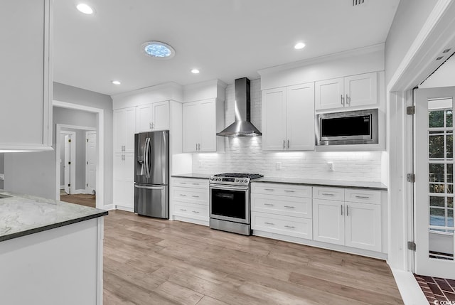 kitchen with white cabinetry, appliances with stainless steel finishes, wall chimney range hood, light stone countertops, and light wood finished floors