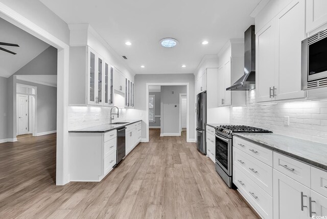 kitchen with light stone counters, wall chimney range hood, stainless steel appliances, and white cabinets