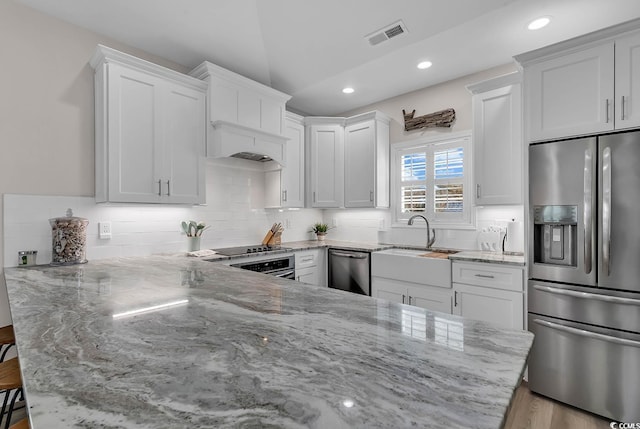 kitchen with white cabinetry, light stone counters, stainless steel appliances, and kitchen peninsula