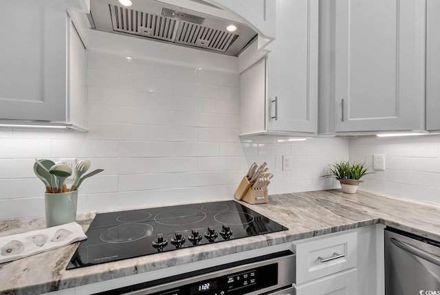 kitchen with white cabinetry, black electric stovetop, light stone counters, and wall chimney exhaust hood