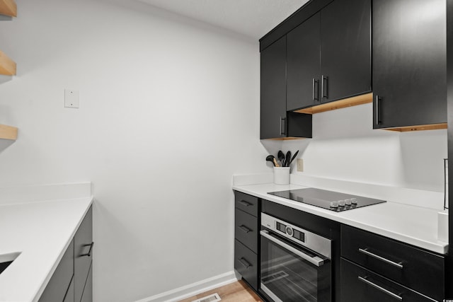 kitchen featuring black electric cooktop, light hardwood / wood-style floors, exhaust hood, and stainless steel oven