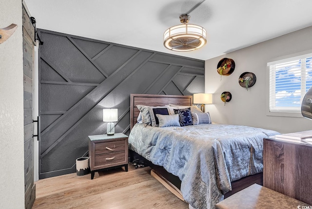 bedroom with a barn door and light wood-type flooring