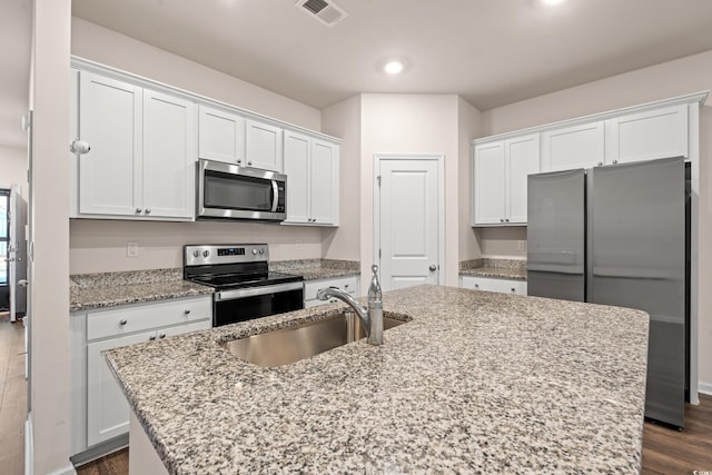 kitchen with sink, appliances with stainless steel finishes, white cabinetry, light stone counters, and a center island with sink