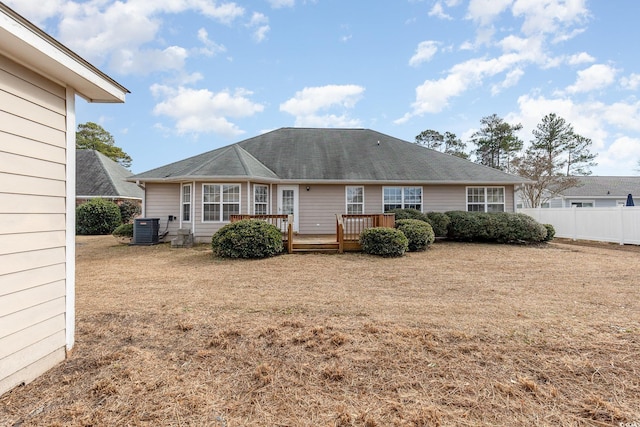 rear view of house with cooling unit, a deck, and a lawn