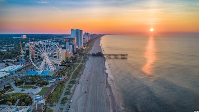 aerial view at dusk featuring a water view and a beach view