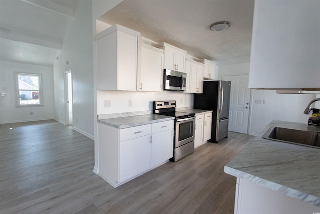 kitchen with appliances with stainless steel finishes, sink, white cabinets, light hardwood / wood-style floors, and a textured ceiling