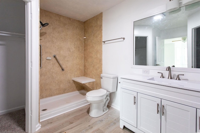 bathroom featuring a tile shower, hardwood / wood-style flooring, vanity, ceiling fan, and toilet