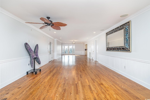 unfurnished living room with a ceiling fan, a wainscoted wall, crown molding, french doors, and light wood-type flooring