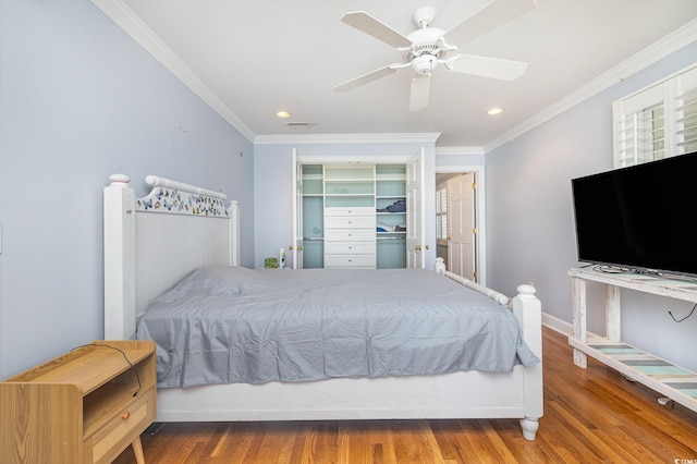 bedroom with baseboards, ceiling fan, wood finished floors, crown molding, and a closet