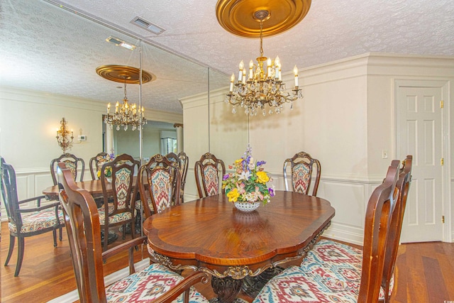 dining room featuring hardwood / wood-style flooring, ornamental molding, a chandelier, and a textured ceiling