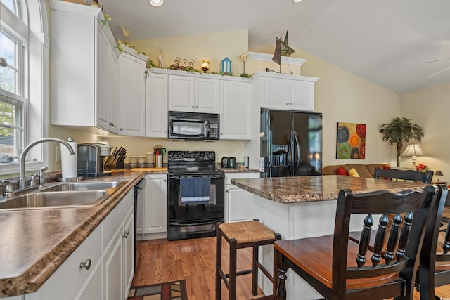kitchen with vaulted ceiling, sink, white cabinets, black appliances, and light wood-type flooring