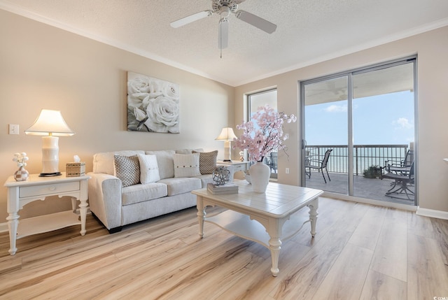 living room featuring ceiling fan, ornamental molding, light hardwood / wood-style floors, and a textured ceiling