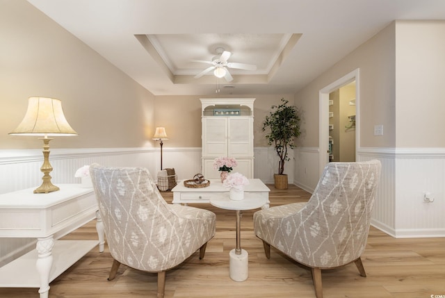 sitting room with a raised ceiling, ceiling fan, and light wood-type flooring