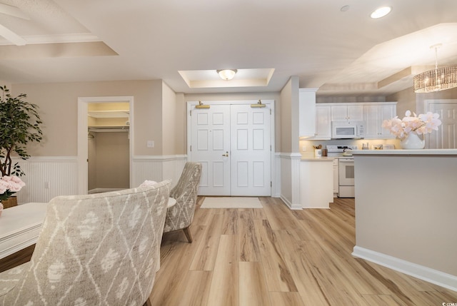 kitchen featuring white appliances, white cabinetry, hanging light fixtures, a tray ceiling, and light wood-type flooring