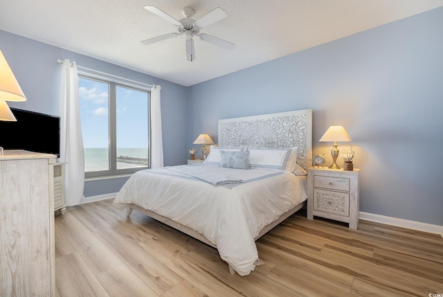 bedroom with a textured ceiling, light hardwood / wood-style floors, and ceiling fan