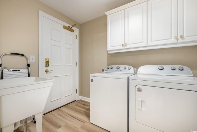 laundry room featuring cabinets, sink, washing machine and clothes dryer, and light hardwood / wood-style floors