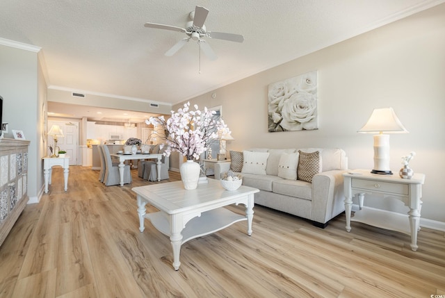 living room featuring ceiling fan, ornamental molding, light hardwood / wood-style floors, and a textured ceiling