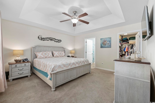 carpeted bedroom with ceiling fan, ensuite bathroom, a raised ceiling, a spacious closet, and a closet