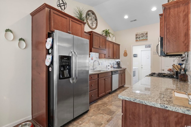 kitchen with appliances with stainless steel finishes, lofted ceiling, sink, decorative backsplash, and light stone counters