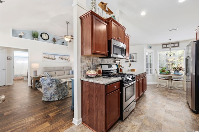 kitchen with ceiling fan with notable chandelier, decorative light fixtures, decorative backsplash, stainless steel appliances, and light stone countertops