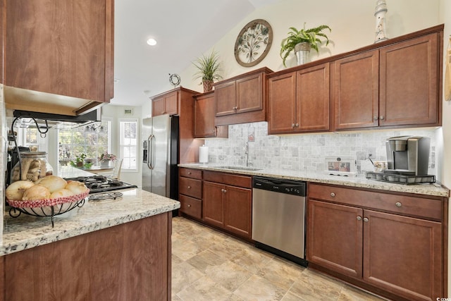 kitchen with vaulted ceiling, appliances with stainless steel finishes, sink, backsplash, and light stone countertops