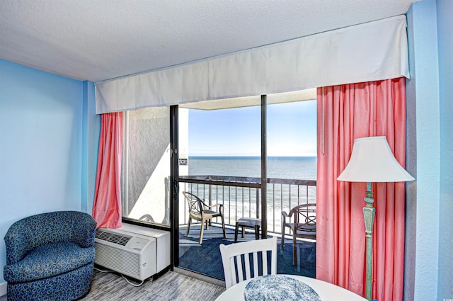 interior space with a water view, a wall unit AC, wood-type flooring, and a textured ceiling