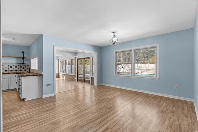 unfurnished living room featuring an inviting chandelier, sink, and light hardwood / wood-style floors