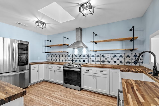 kitchen featuring wall chimney exhaust hood, stainless steel appliances, butcher block counters, and white cabinets