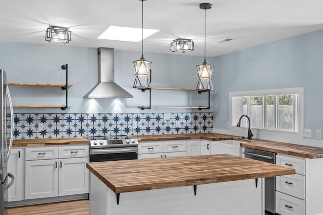 kitchen featuring pendant lighting, appliances with stainless steel finishes, range hood, white cabinets, and wood counters