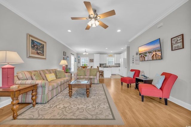 living area featuring baseboards, light wood-style flooring, recessed lighting, crown molding, and ceiling fan with notable chandelier