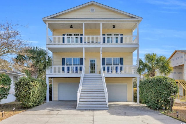 raised beach house with a porch, stairs, a balcony, a garage, and driveway