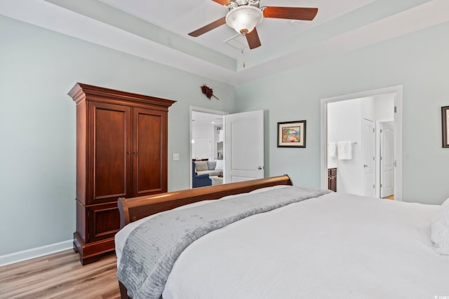 bedroom featuring ceiling fan, connected bathroom, a tray ceiling, and light wood-type flooring