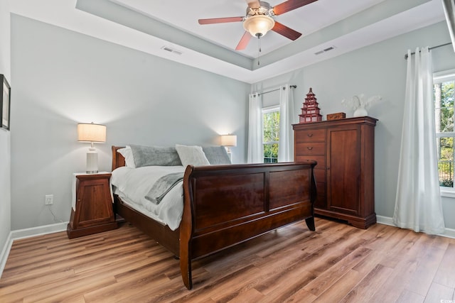 bedroom featuring a raised ceiling, multiple windows, and light wood-type flooring