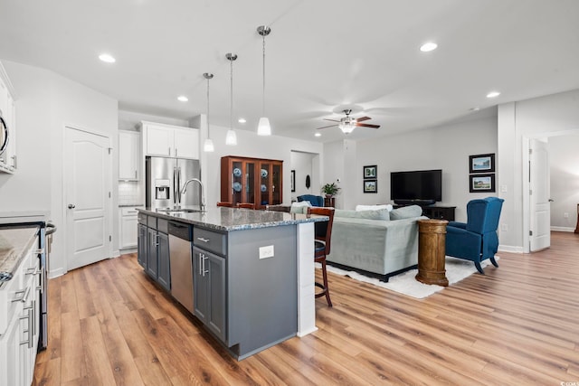 kitchen featuring gray cabinetry, hanging light fixtures, stainless steel appliances, a kitchen island with sink, and white cabinets