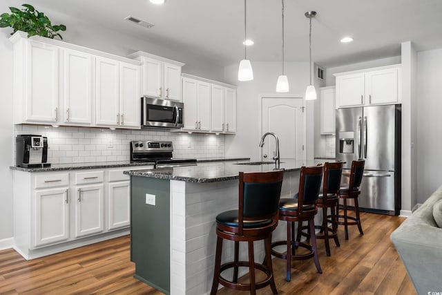 kitchen with appliances with stainless steel finishes, decorative light fixtures, an island with sink, sink, and white cabinets