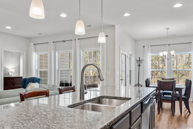 kitchen featuring sink, a wealth of natural light, light stone counters, and decorative light fixtures