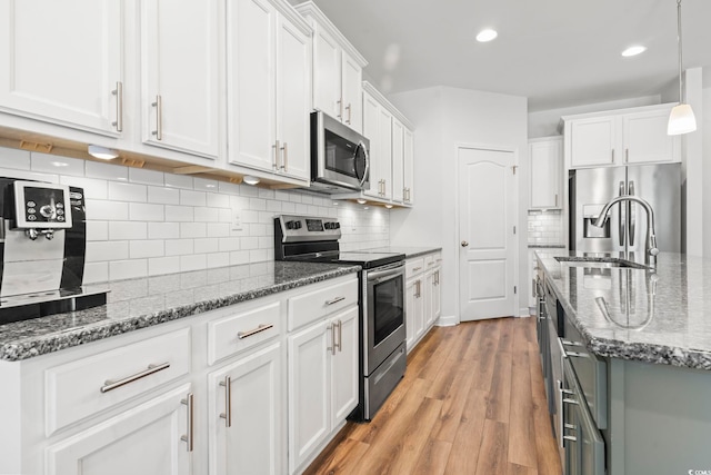 kitchen featuring sink, appliances with stainless steel finishes, white cabinetry, dark stone countertops, and light hardwood / wood-style floors