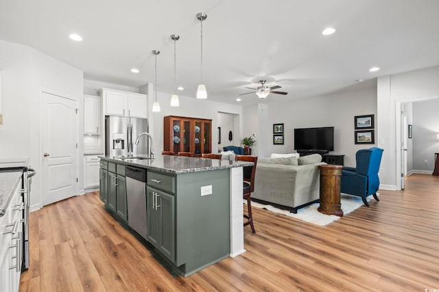 kitchen with light hardwood / wood-style flooring, appliances with stainless steel finishes, a kitchen island with sink, white cabinets, and decorative light fixtures