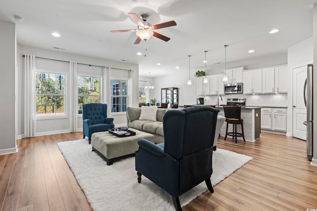 living room with sink, ceiling fan with notable chandelier, and light hardwood / wood-style flooring