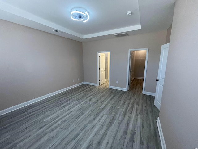 unfurnished bedroom featuring hardwood / wood-style floors, a tray ceiling, and a walk in closet