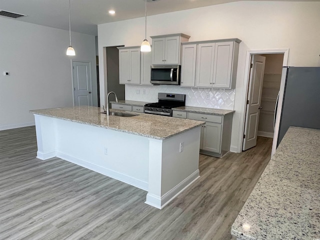 kitchen with sink, hanging light fixtures, stainless steel appliances, tasteful backsplash, and a center island with sink