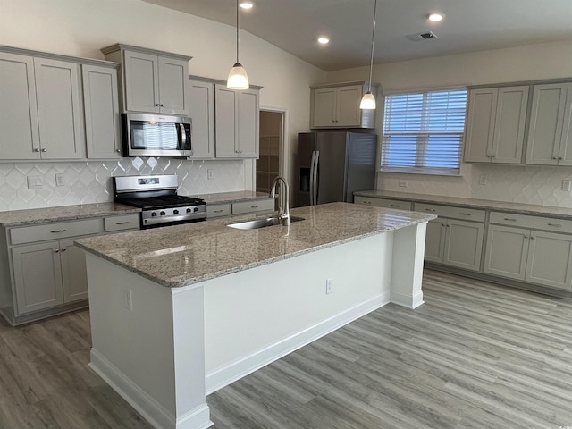 kitchen with sink, hanging light fixtures, an island with sink, stainless steel appliances, and light stone countertops