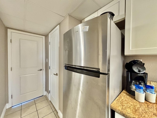 kitchen with white cabinets, freestanding refrigerator, light stone countertops, a paneled ceiling, and light tile patterned flooring