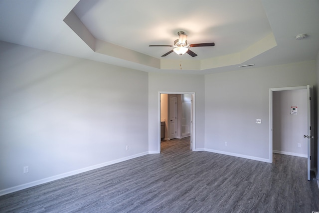 empty room featuring visible vents, a raised ceiling, dark wood-style floors, baseboards, and ceiling fan