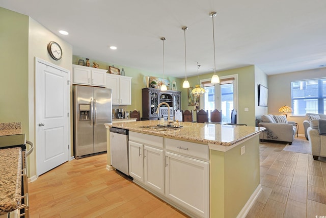 kitchen featuring sink, decorative light fixtures, appliances with stainless steel finishes, a kitchen island with sink, and white cabinets