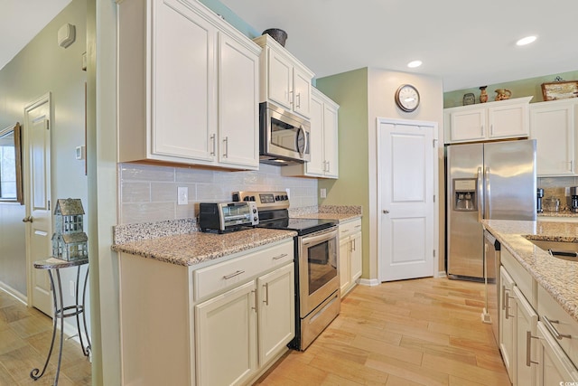 kitchen with stainless steel appliances, light stone countertops, white cabinets, and light hardwood / wood-style flooring