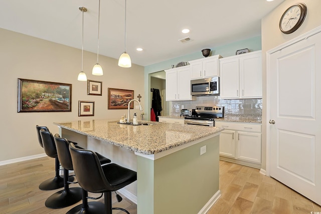 kitchen featuring white cabinetry, an island with sink, appliances with stainless steel finishes, and pendant lighting