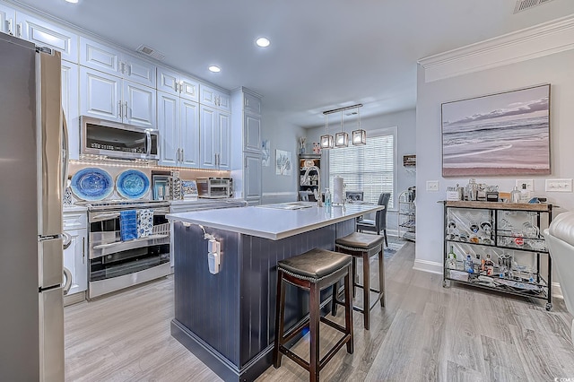 kitchen with a breakfast bar area, appliances with stainless steel finishes, white cabinetry, hanging light fixtures, and a center island with sink