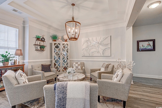 living room featuring hardwood / wood-style flooring, crown molding, a raised ceiling, and a notable chandelier